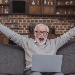 Happy grey hair man watching on laptop at home and celebrate win a bet with a gambling, soccer bet,