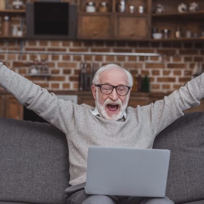 Happy grey hair man watching on laptop at home and celebrate win a bet with a gambling, soccer bet,