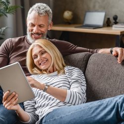 Happy senior couple using digital tablet on sofa indoors